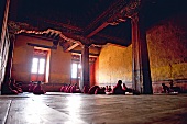 Young monks sitting in prayer hall of Paro Dzong monastery and reading prayer, Bhutan