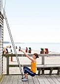 Side view of young woman in sportswear exercising with support of cable squat on beach