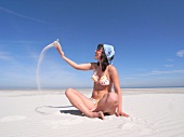 Woman wearing bikini playing with sand on beach, smiling