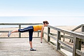 Side view of woman in sportswear holding dumbbells performing deadlift exercise on beach