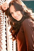 Portrait of beautiful dark haired woman wearing brown turtleneck leaning against wall