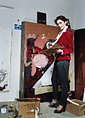 Frau brünett, Blazer rot, steht, malt Bild, Atelier, Kamerablick