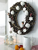 Wooden Christmas wreath hanging on white wall with white wool pom poms