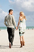 Couple holding hand and walking on beach, smiling