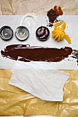 Baking paper, liquid chocolate, moulds and orange on baking paper