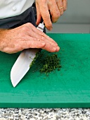 Chopping green fennel leaves on cutting board with knife