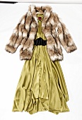 Close-up of faux fur coat with collar over green silk dress on white background