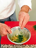 Close-up of man's hands adding ingredients while preparing pine nut vinaigrette
