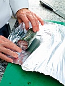 Rolled screw beef in cling film being rolled in aluminium foil