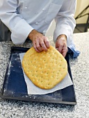 Man's hands removing baked focaccia bread from the baking sheet