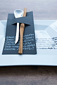 Setting of cutlery on black cardboard with epigraphy on dish