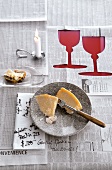 Newspaper spread as tablecloth with cheese, lit candle and two cup shaped cut out