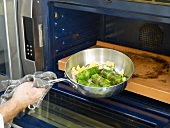 Close-up of man's hand putting pan with stuffed cabbage rolls in oven