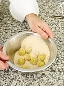 Close-up of man's hands coating fried rice balls in bowl