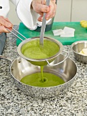 Close-up of man's hands straining green puree with strainer in pan
