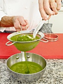 Green puree being strained through strainer in pan