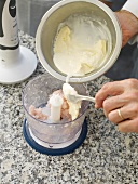 Cream being added to minced fish in blender while preparing fish farce
