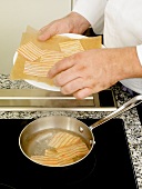 Putting cut pieces of lasagna pasta in saucepan with oil