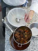 Straining brown veal mixture with colander in pan
