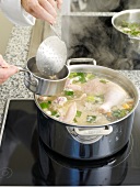 Skimming from chicken stock mixture in pot