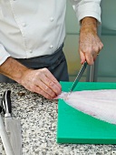 Cutting caudal fin of sole by knife on chopping board
