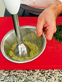 Close-up of mixture being blended with hand blender for pine nut vinaigrette