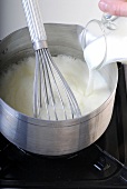 Milk being added in sauce pan with whisk for preparing bechamel sauce, step 2