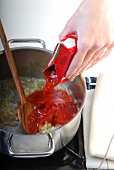 Tomato puree added to frying onions in casserole with wooden spoon, step 2