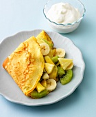 Cream in bowl and folded pancakes with fruit salad on plate