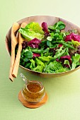 A mixed leaf salad in a wooden bowl with a dressing