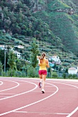 Junge Frau im Sportdress läuft auf der Tartanbahn