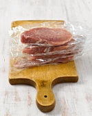 Schnitzel individually wrapped in transparent foil on wooden board