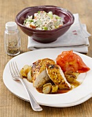 Chicken with tomato on plate and bowl of lettuce salad in background