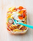 Pasta salad with vegetables and ham in a plastic box