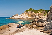 People relaxing under parasol on rocks at Capo Sant'Andrea, Tuscany, Italy