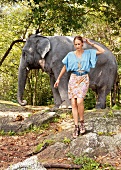 Pretty woman wearing top with kimono sleeves and skirt standing in front of elephant