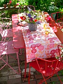 Dining table and chairs in pink and red with flower bouquet in garden