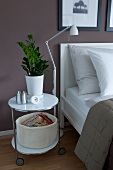 White side table with house plant in pot besides bed and floor lamp