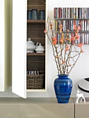 Hanging cabinet, CD racks, flower branches in blue vase in room