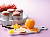 Peeled orange on chopping board and cupcakes on tray
