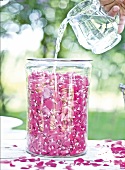 Water being poured in glass jar with rose petals