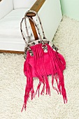 Pink fringed handbag with snake patterned handle on white carpet