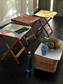 Folding stool covered with colourful fabrics and basket of fruits on wooden floor