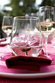 Pink flower in wine glass on red napkin, overhead view