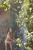 Junge Frau in Slip und Bikini duscht im Freien vor einer Felswand