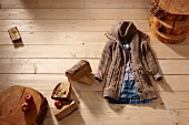 Brown jacket and denim skirt arranged on floor with cut wood and apples on wooden floor