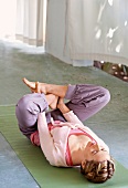 Woman lying in supine position on exercising mat with feet crossed, performing yoga