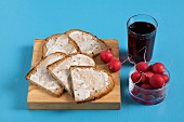 Slices of coated bread on wood, radish in bowl and juice glass on blue background