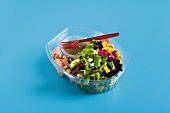 Vegetable salad with tuna in disposable plastic container on blue background