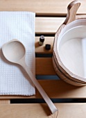 Wooden container with essential oil and wooden spoon on tissue, overhead view